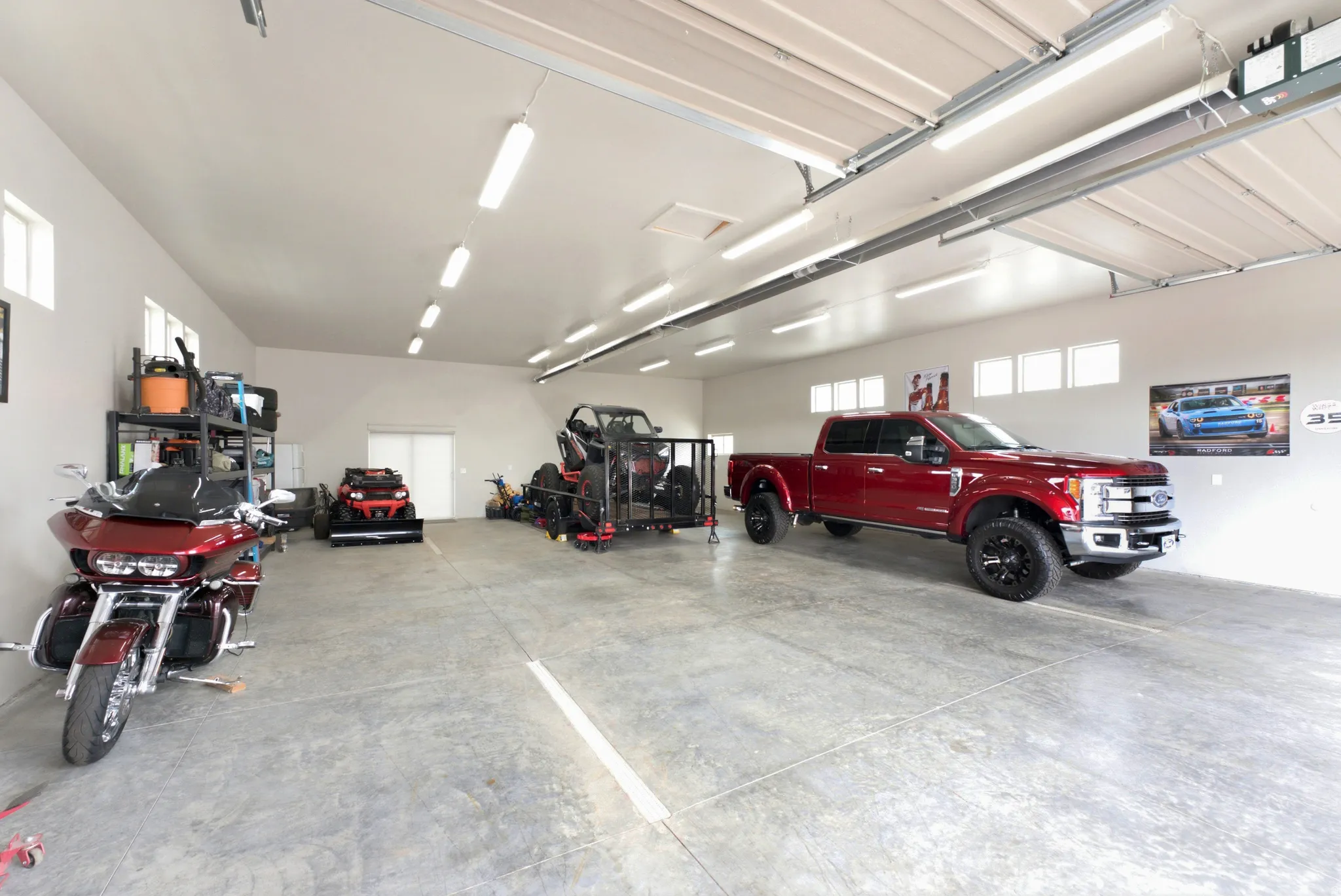 Spacious garage featuring concrete flooring, abundant overhead strip lighting, multiple high-set windows, and a roll-up door