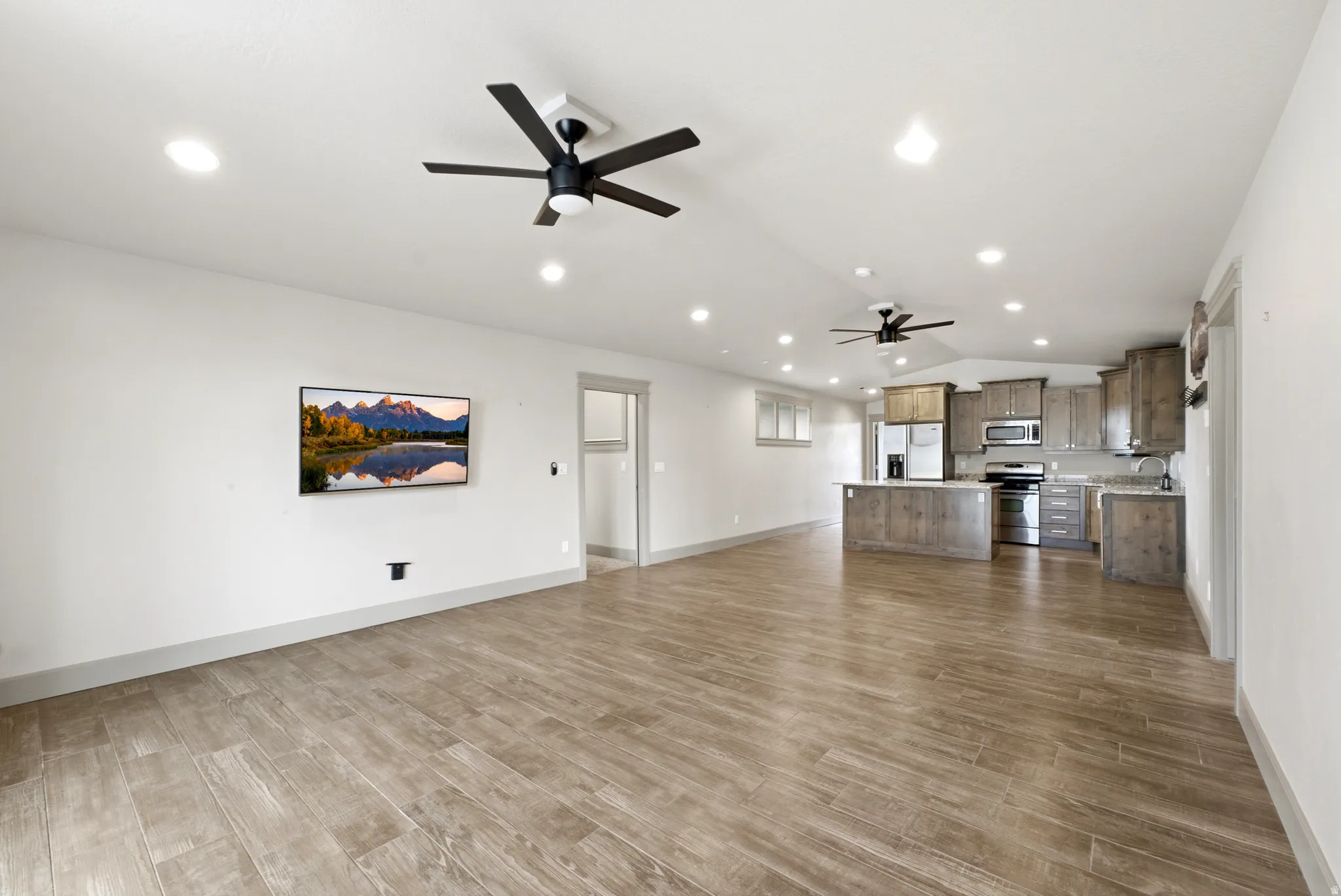 Open-concept living area featuring wood-finish flooring throughout, recessed ceiling lighting, and dual ceiling fans