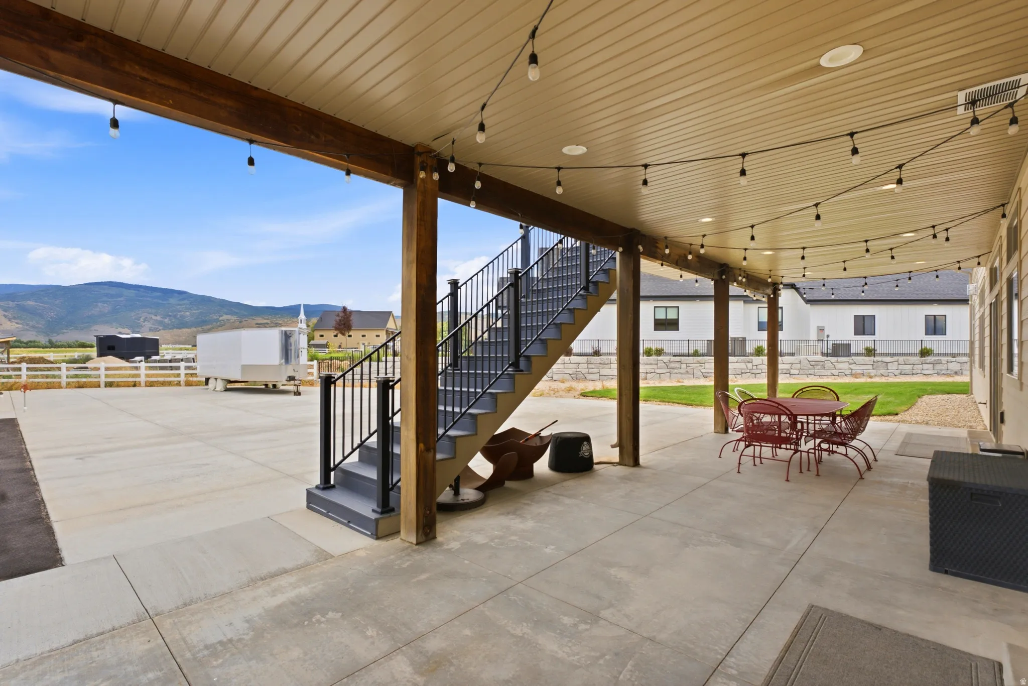 Expansive concrete patio with wood-tone support beams and string lighting