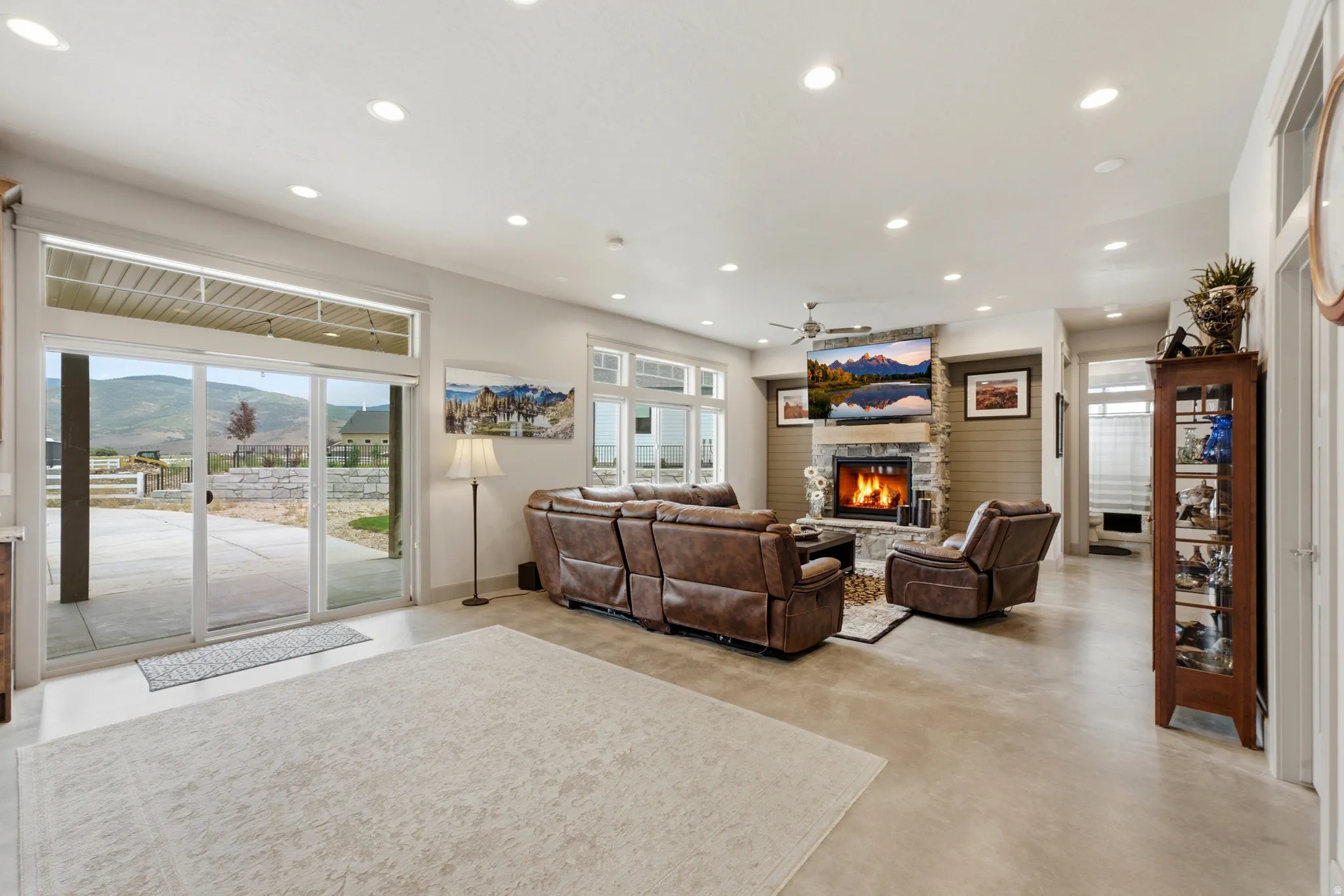 Living area featuring a stone fireplace with a wood mantle, a ceiling fan, recessed lighting, and sliding glass doors to the outdoor patio