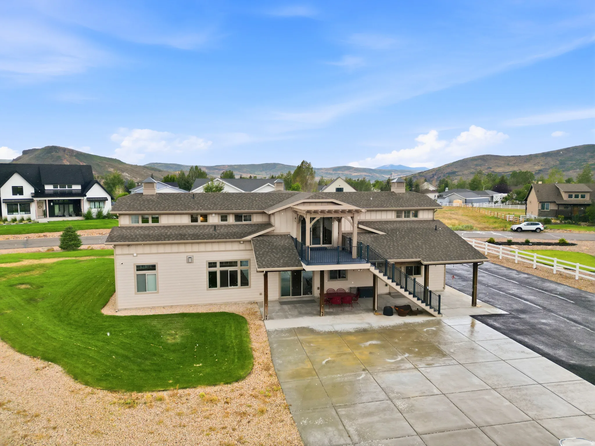 Multi-level residence featuring a large concrete patio, a covered outdoor area, and an upper-level balcony with railings