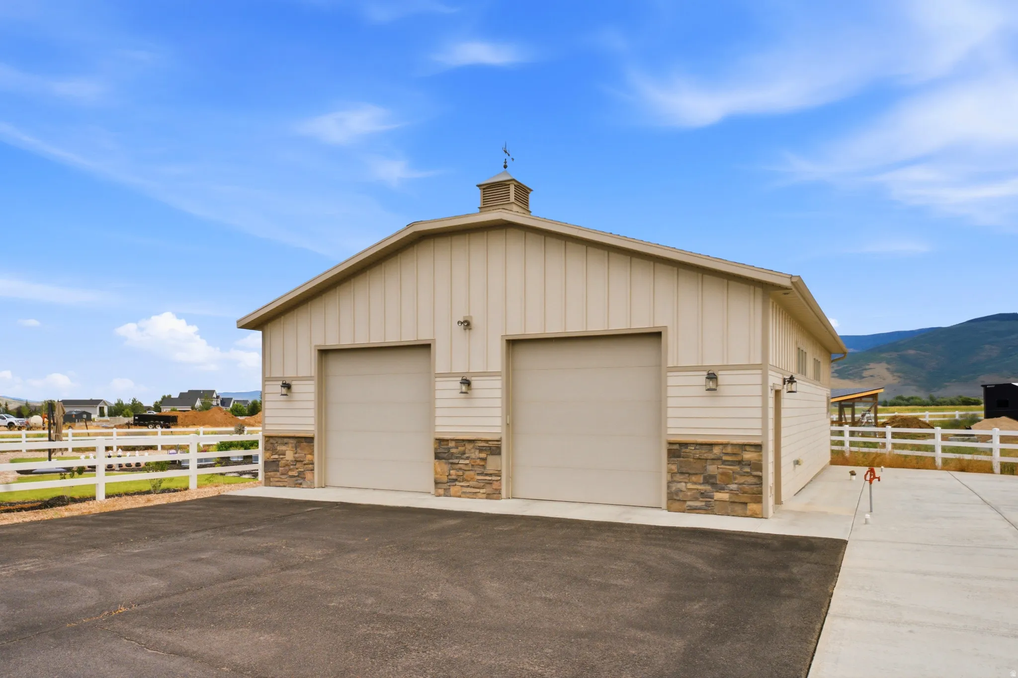 Modern agricultural garage featuring two oversized bay doors with steel frames, stone veneer accents along the foundation, standing-seam metal siding in neutral tones, and a peaked roofline with cupola detail
