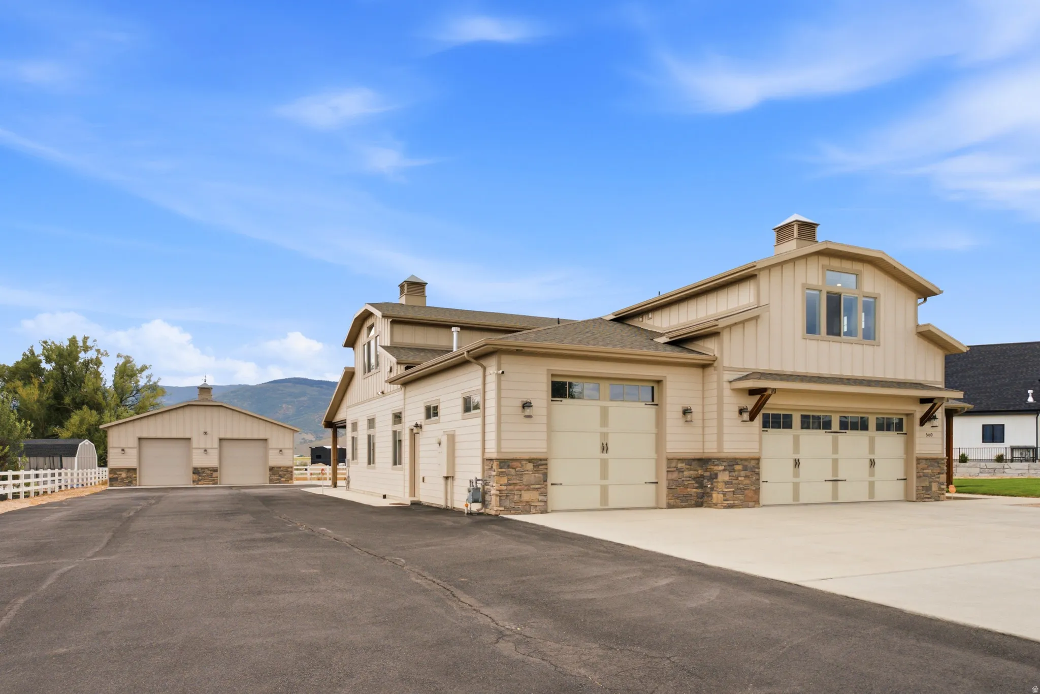 Impressive residential compound featuring a substantial two-story residence with stone and stucco exterior, multiple garage bays with overhead doors, and expansive paved driveway
