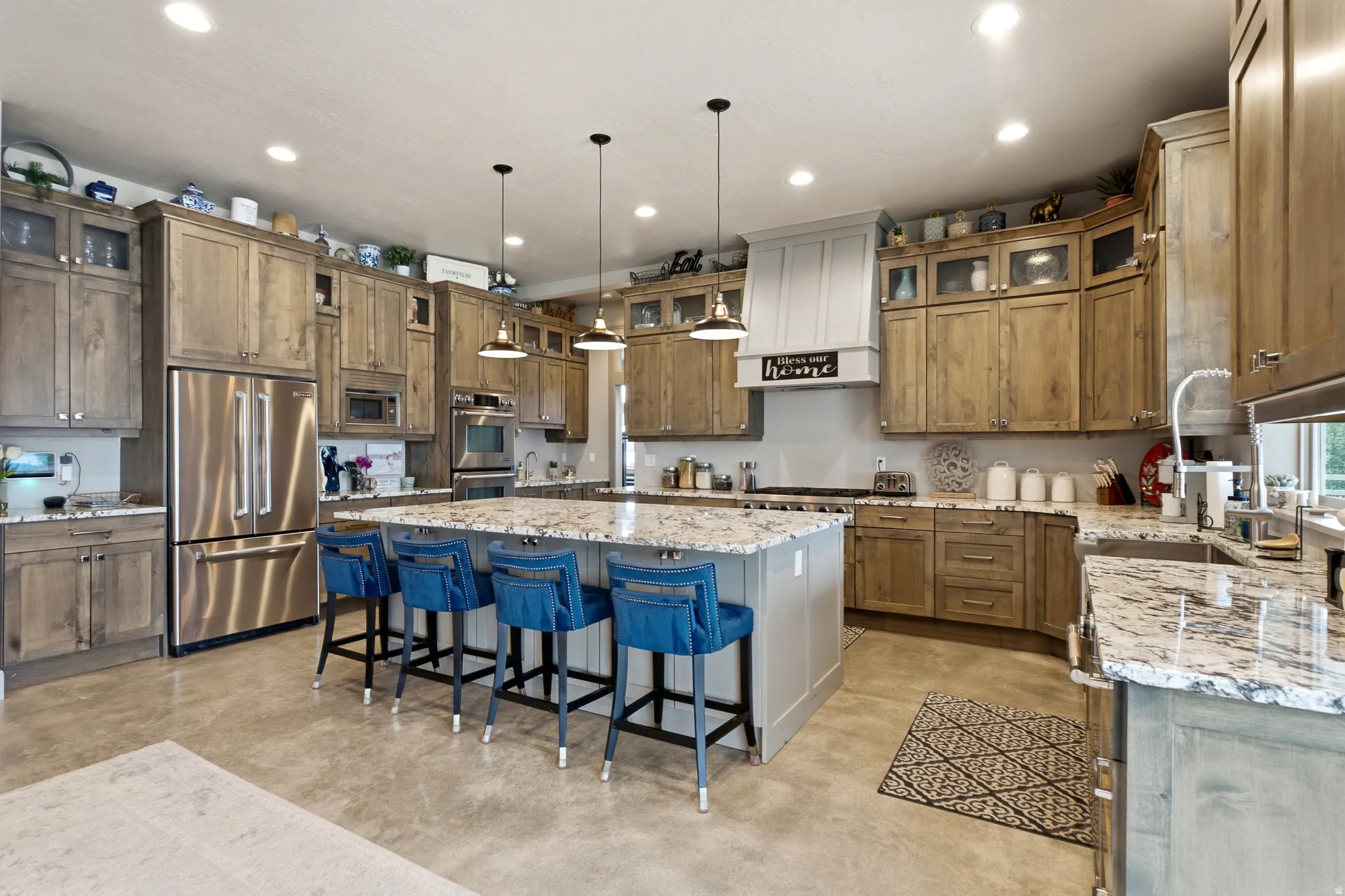 Chef's kitchen featuring custom wood cabinetry, stainless steel appliances, granite-topped island with seating for multiple, pendant lighting, and expansive countertop workspace