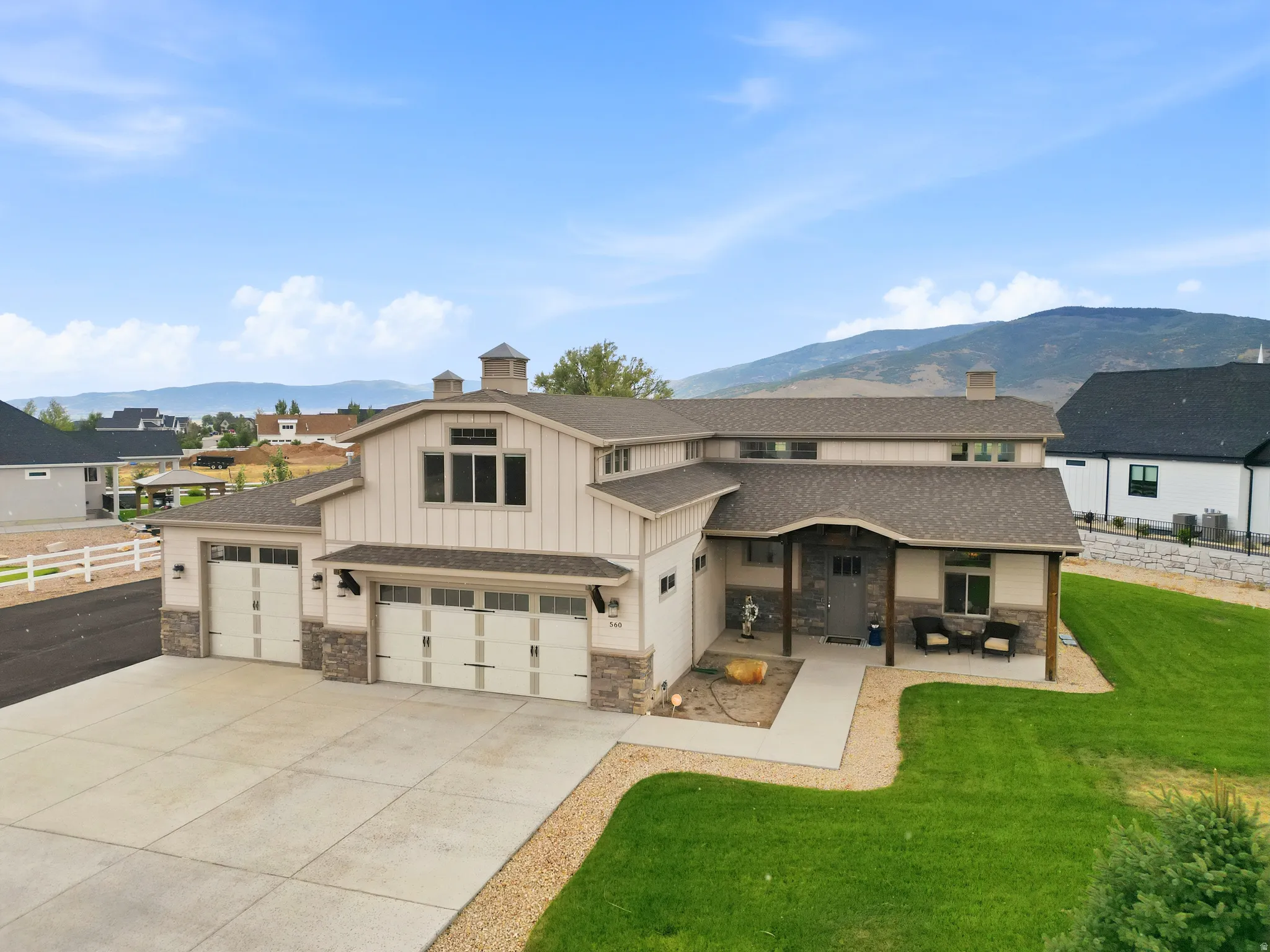 Two-story residence featuring a triple-car garage, stone and siding exterior, covered porch entry, and a manicured lawn