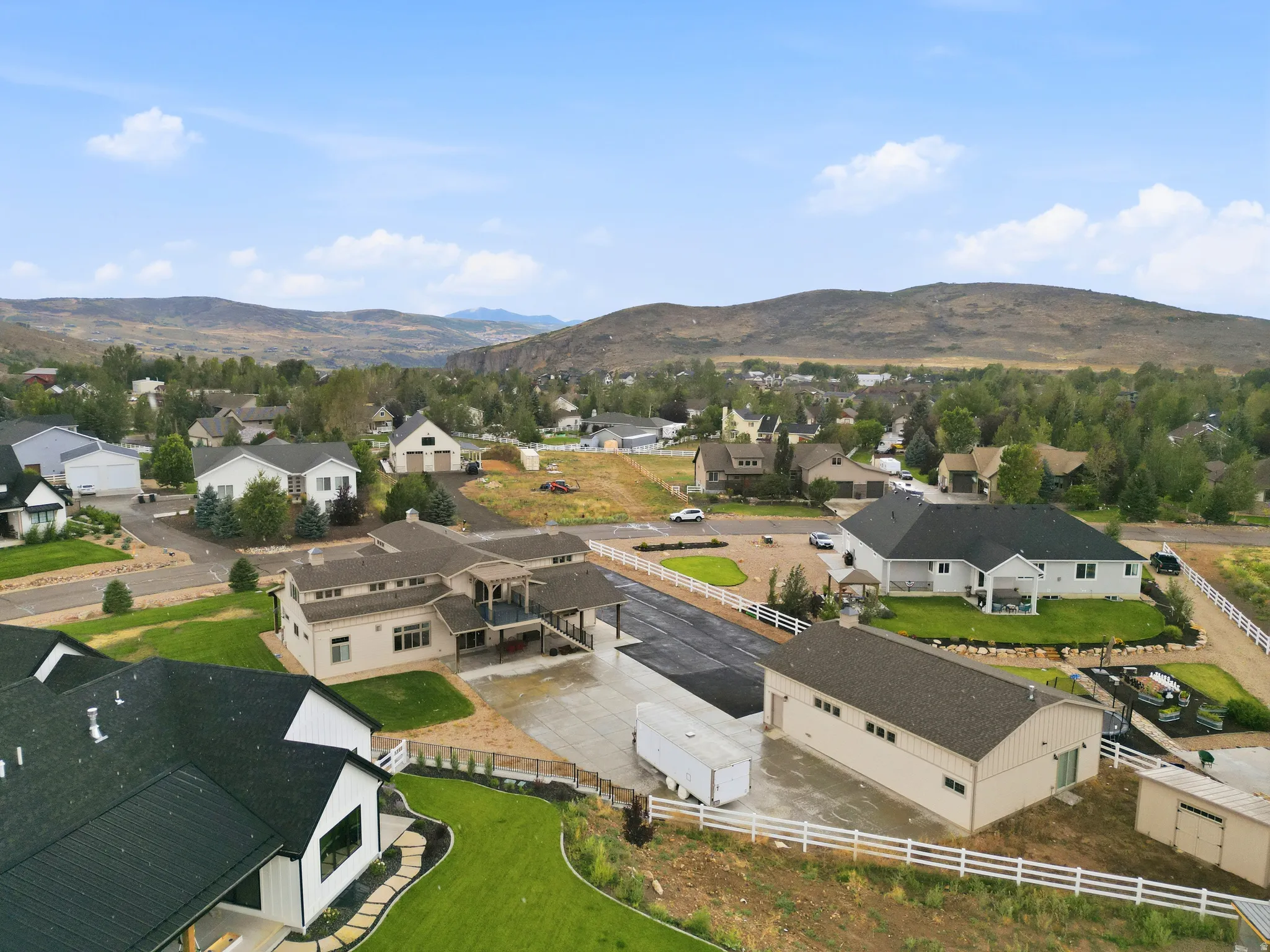 Expansive property featuring a large residence, separate detached building, paved driveways, and manicured landscaping with white fencing