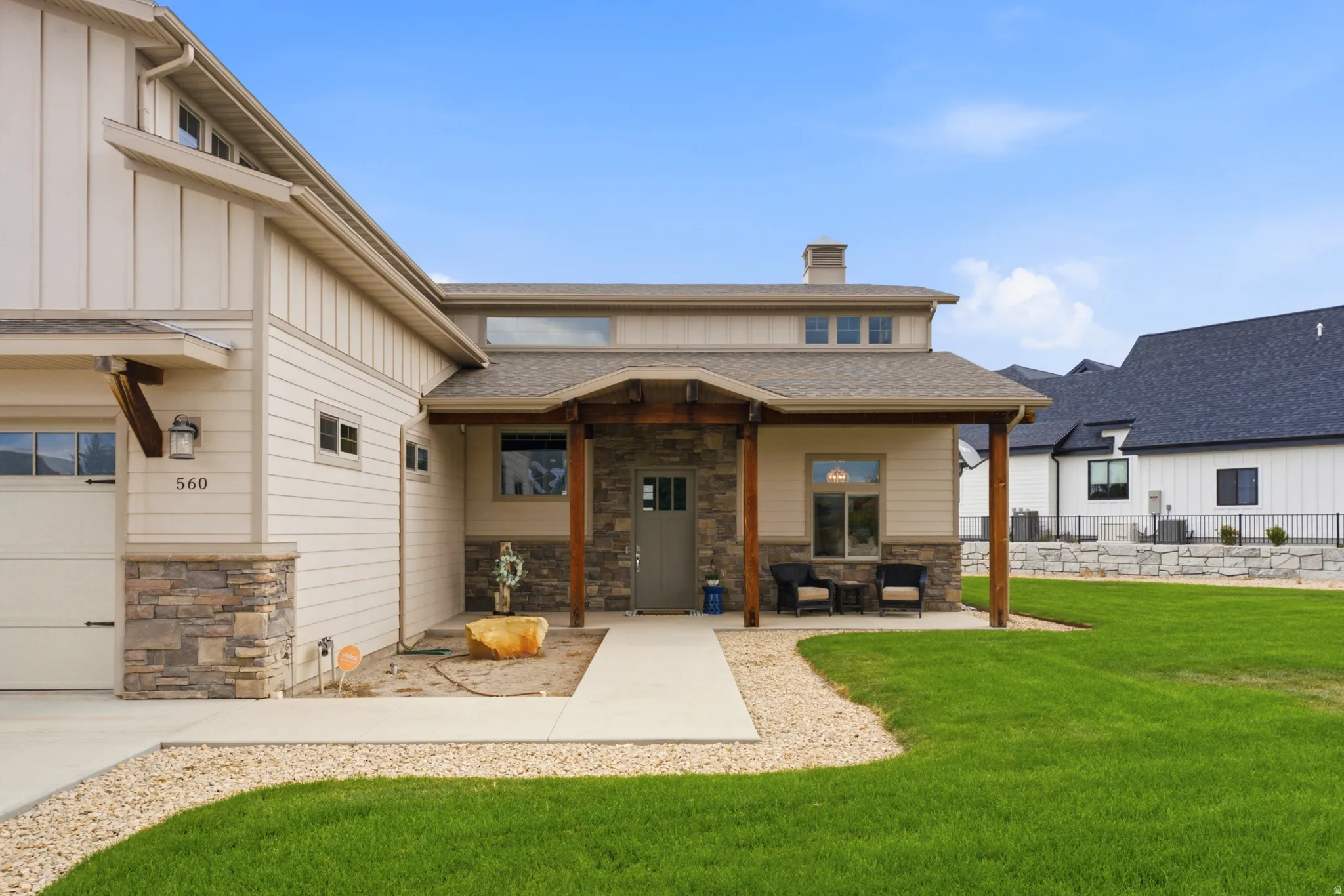 Stone veneer accents on the facade, covered front entry porch, wood-finish columns, board and batten siding, and a concrete pathway