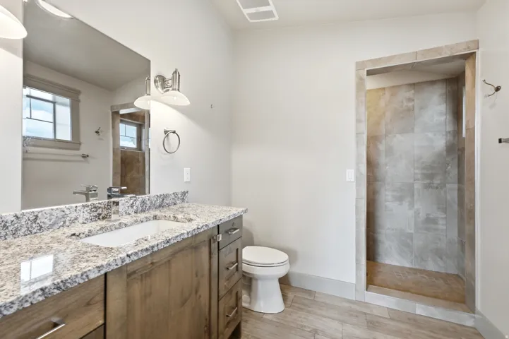 Granite-style countertop with integrated sink, wood-finish vanity, and a tiled shower stall