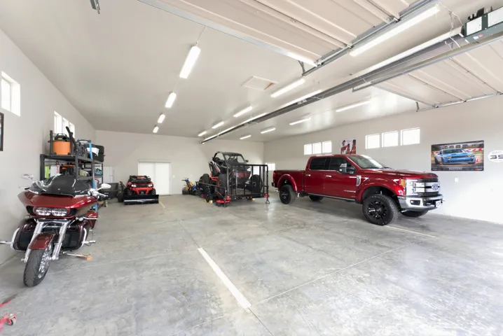 Spacious garage featuring concrete flooring, abundant overhead strip lighting, multiple high-set windows, and a roll-up door