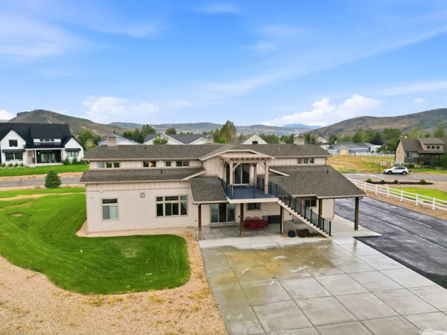 Multi-level residence featuring a large concrete patio, a covered outdoor area, and an upper-level balcony with railings