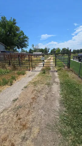 Secured property entrance featuring a metal gate, gravel driveway, and perimeter fencing