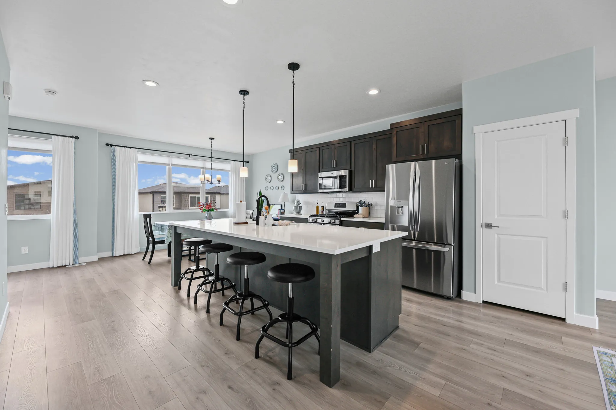 Kitchen featuring a large island with white countertop, dark wood-finish cabinetry, stainless steel appliances, and wood-finish flooring