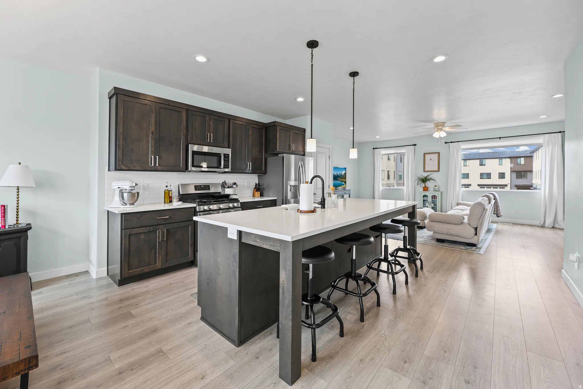 Modern kitchen with dark wood-finish cabinetry, stainless steel appliances, white subway tile backsplash, and a large central island with pendant lighting