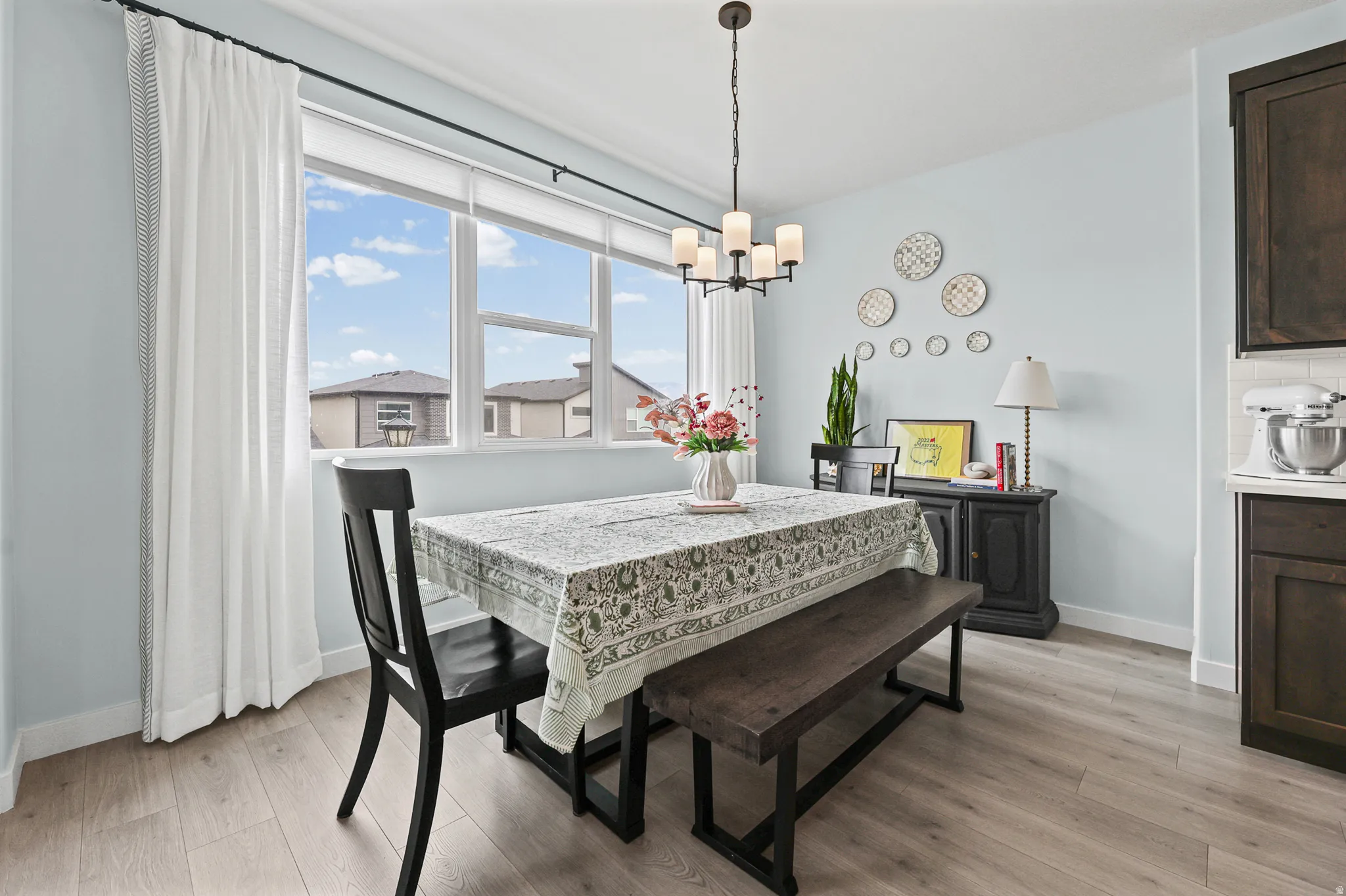 Expansive window with roller shade, wood-finish flooring, dark wood cabinetry, subway tile backsplash, and a modern chandelier