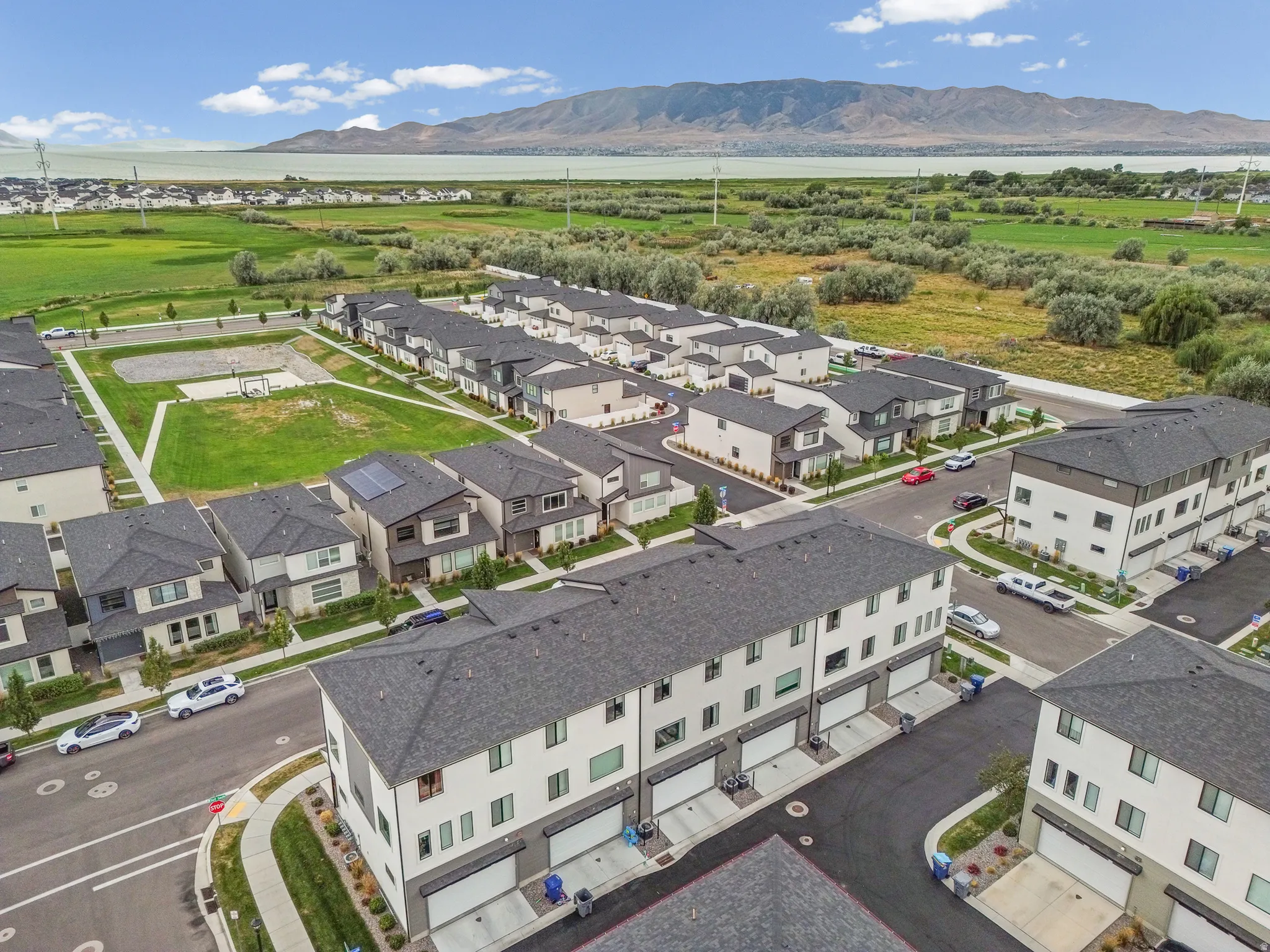 Newly constructed residences with modern exterior finishes, attached garages, and a community green space