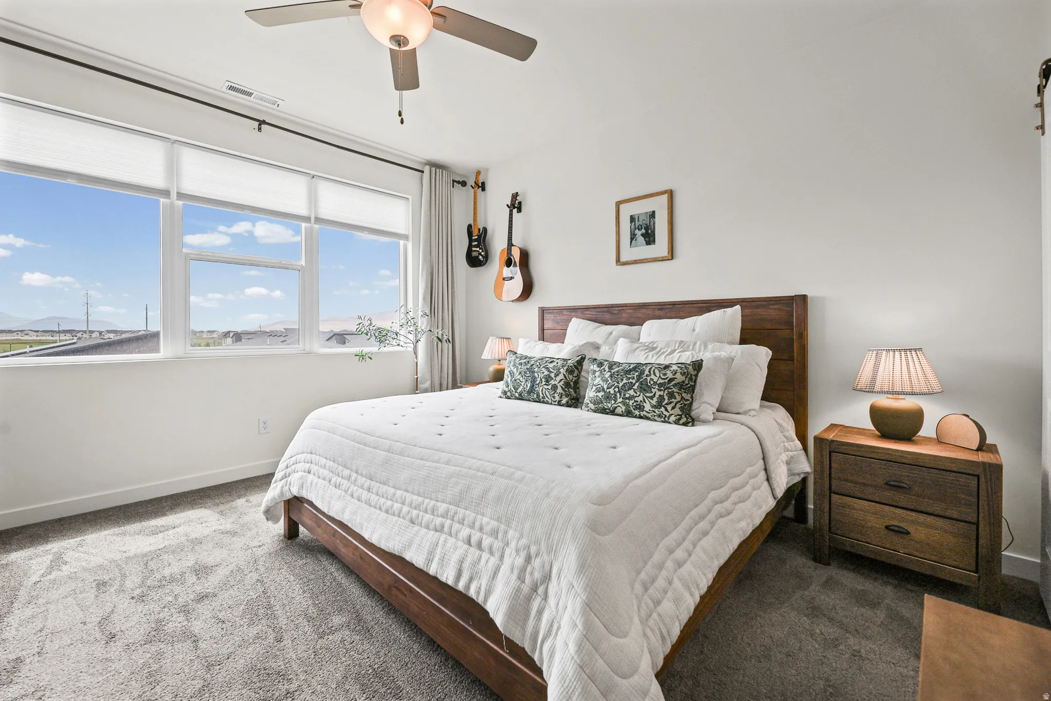 Expansive window wall with roller shades, ceiling fan with integrated lighting, and textured carpet flooring