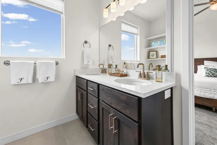 Dual vanity with white undermount sinks and bronze-finish faucets, set in a dark wood-finish cabinet with white countertops