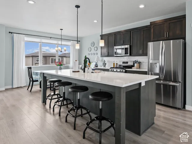 Kitchen featuring a large island with white countertop, dark wood-finish cabinetry, stainless steel appliances, and wood-finish flooring