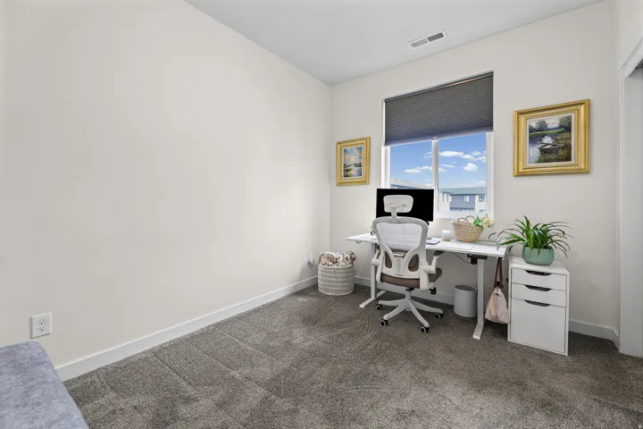 Dedicated home office featuring a large window with natural light, gray carpet flooring, and built-in white cabinetry with storage drawers
