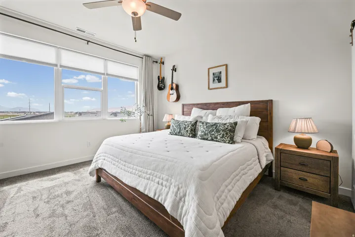 Expansive window wall with roller shades, ceiling fan with integrated lighting, and textured carpet flooring