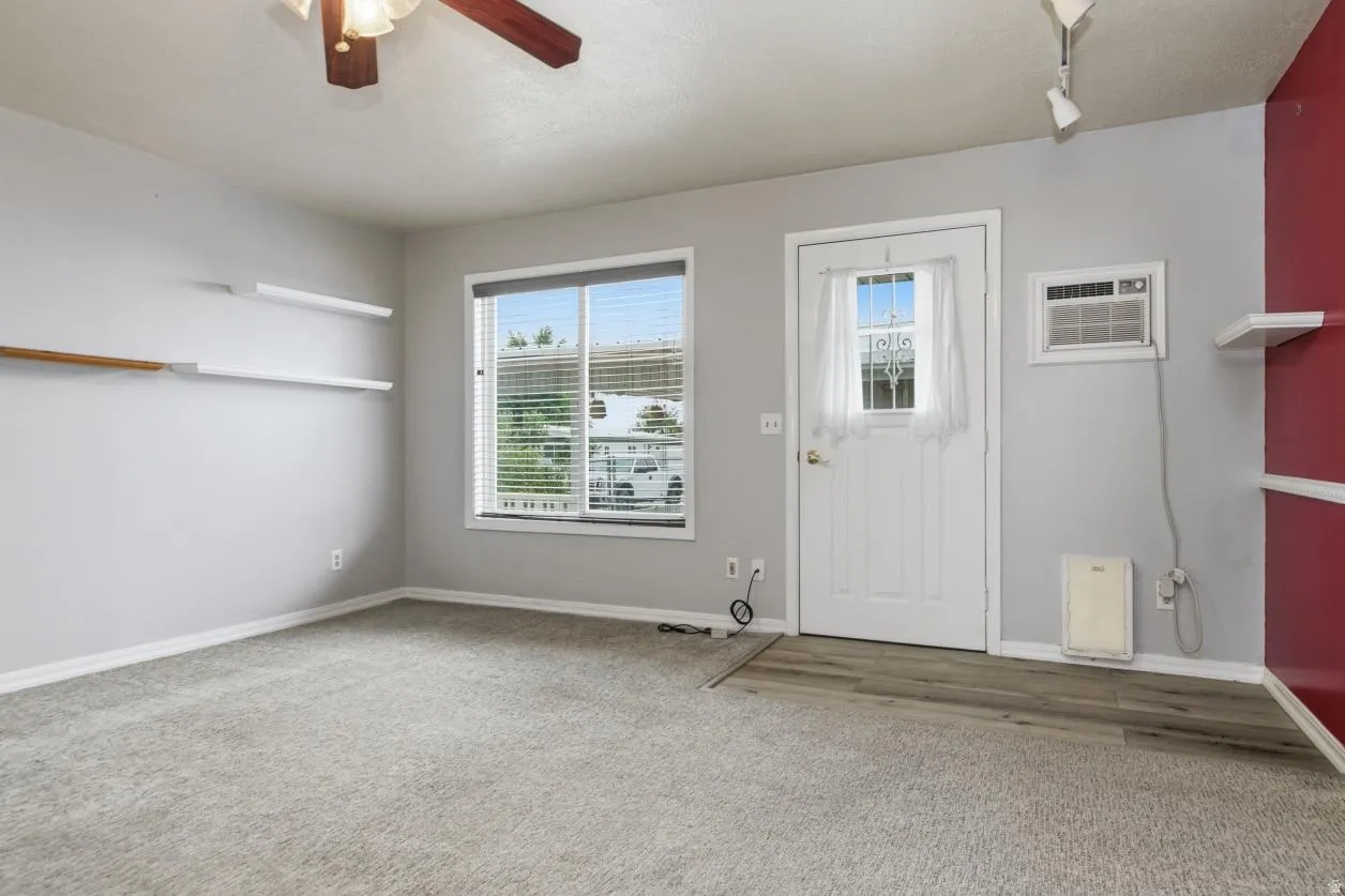 Window with blinds, ceiling fan, wood-finish flooring, wall-mounted shelving, and window air conditioning unit leading to the backyard