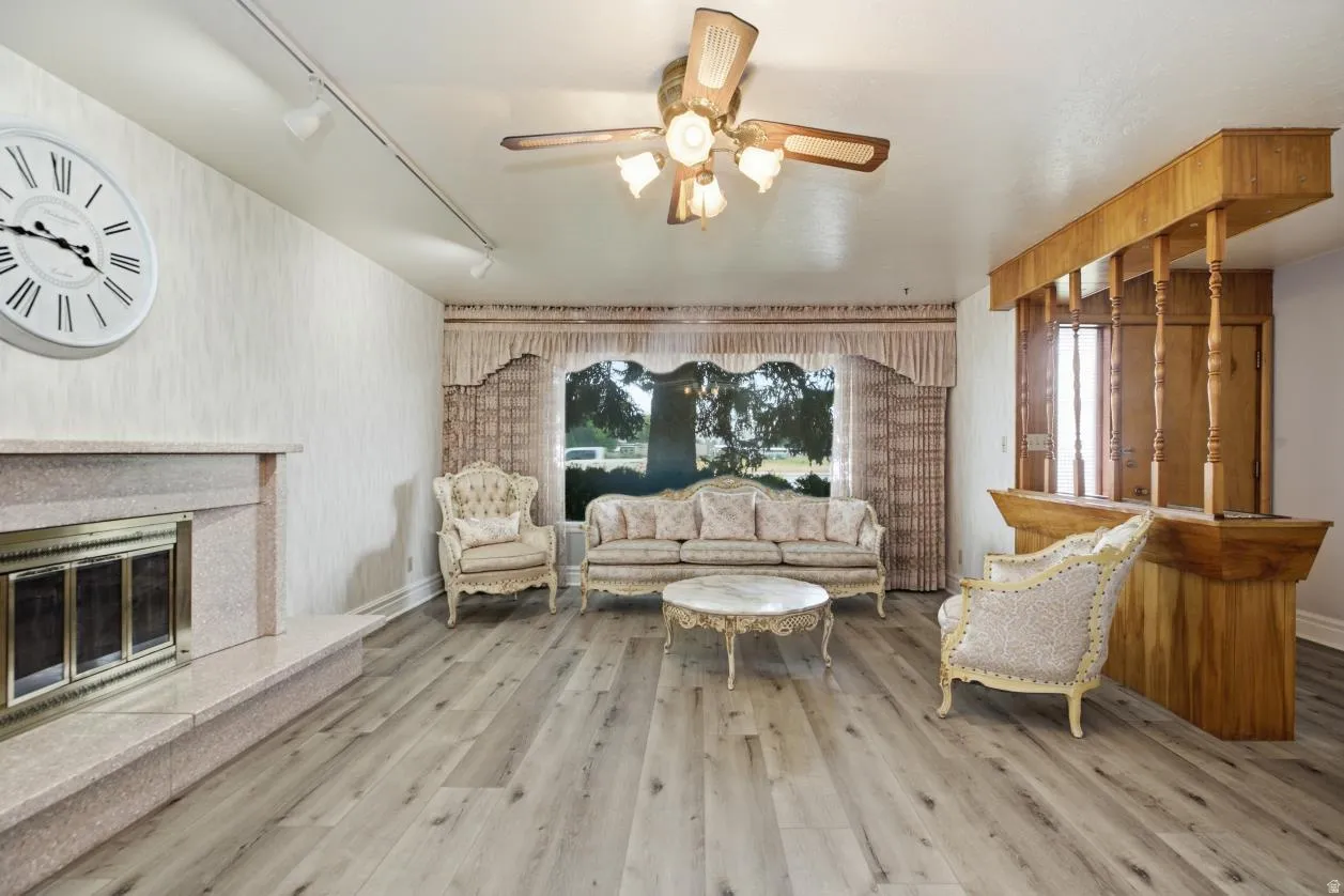 Recessed fireplace with hearth, wood-finish flooring, built-in wooden bar, and a ceiling fan with integrated lighting