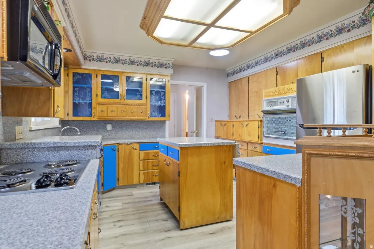 Kitchen featuring a central island, wood-finish cabinetry with some blue panels, light-toned countertops, and a built-in oven with a microwave above