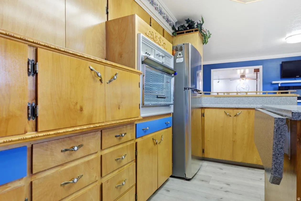 Wood-finish flooring, light wood cabinetry, blue accent cabinetry, built-in wall oven, and granite-look countertops