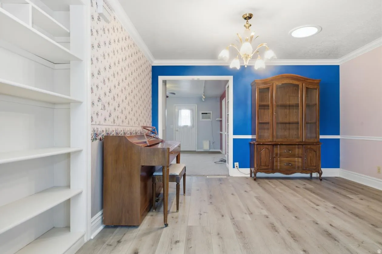 Wood-finish flooring, built-in shelving, crown molding, and an overhead chandelier