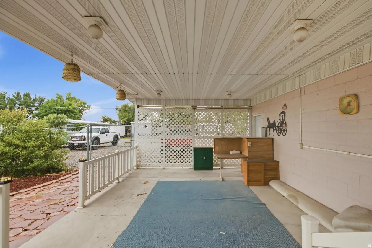 Covered patio with a slatted ceiling, block wall, and white lattice fencing