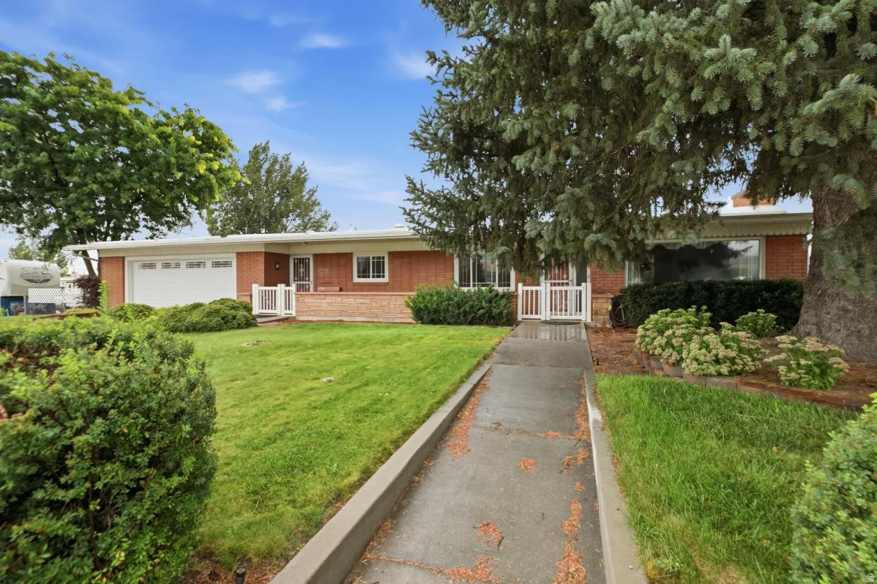 Brick exterior with a white garage door, concrete walkway, and mature landscaping