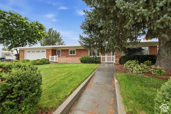 Brick exterior with a white garage door, concrete walkway, and mature landscaping