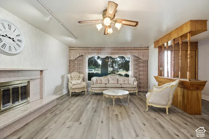 Recessed fireplace with hearth, wood-finish flooring, built-in wooden bar, and a ceiling fan with integrated lighting