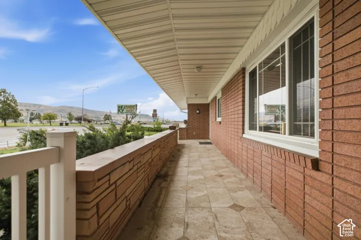 Brick exterior, covered walkway, tiled flooring with accent patterns, white railing, and multiple windows with grids