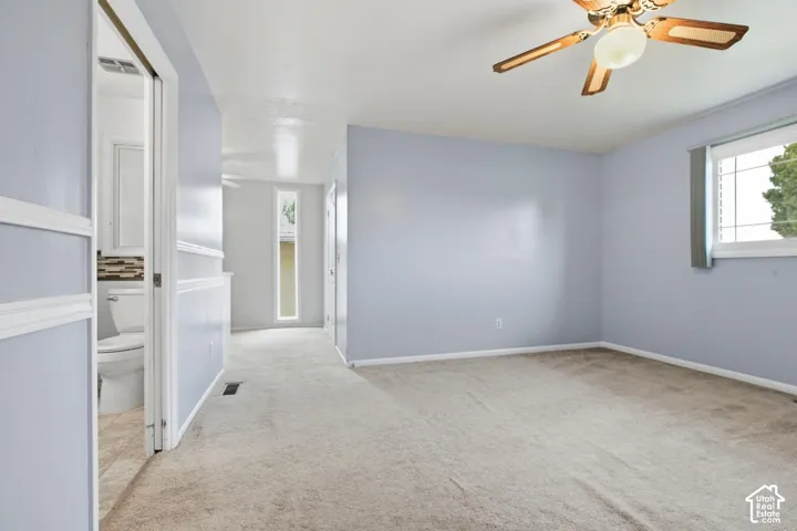 Carpeted flooring, ceiling fan with integrated lighting, natural light from a window, and an adjacent bathroom with tiled flooring and a tiled backsplash