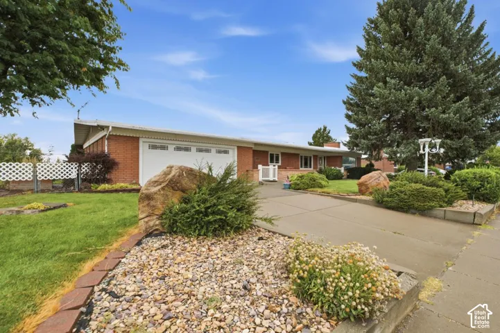 Brick exterior featuring a two-car garage with white door, concrete driveway, and mature landscaping with decorative rock beds