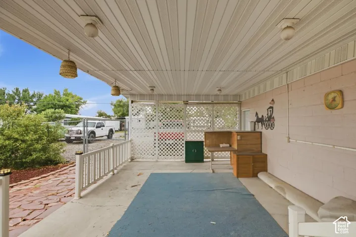 Covered patio with a slatted ceiling, block wall, and white lattice fencing