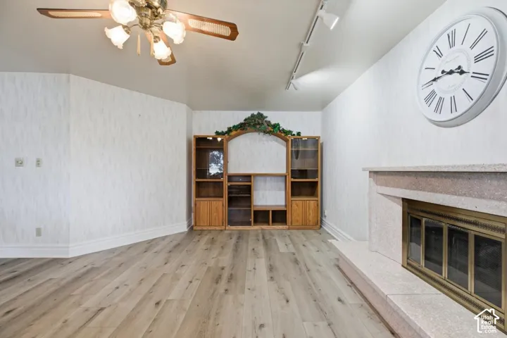 Wood-finish flooring, built-in entertainment center, ceiling fan, track lighting, and a stone-clad fireplace
