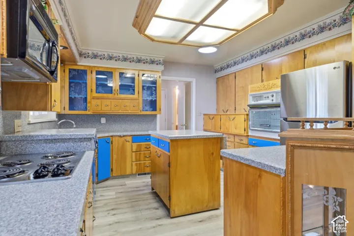 Kitchen featuring a central island, wood-finish cabinetry with some blue panels, light-toned countertops, and a built-in oven with a microwave above
