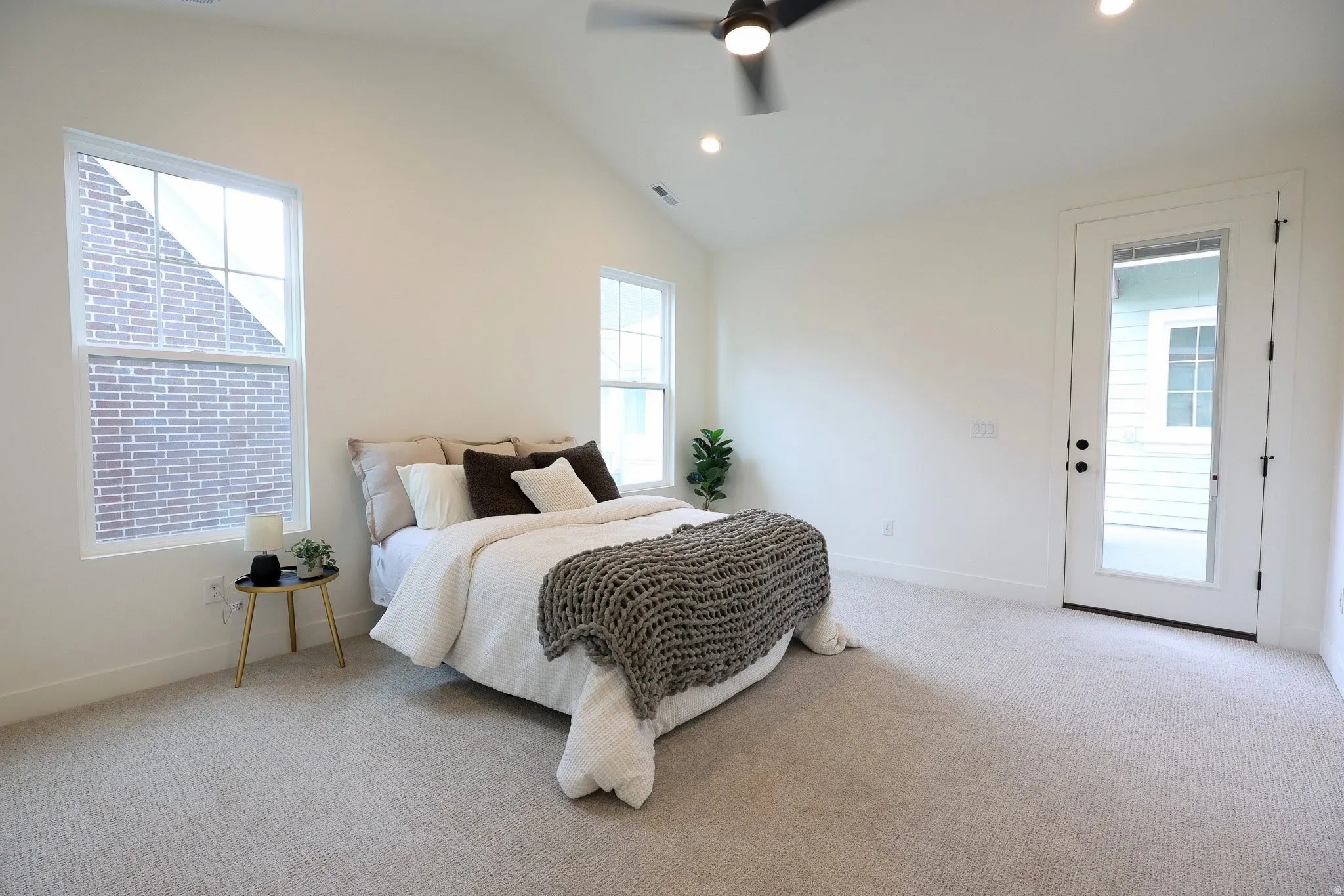 Primary bedroom with Vaulted ceiling, two large windows, white walls, ceiling fan, and a glass-paneled door
