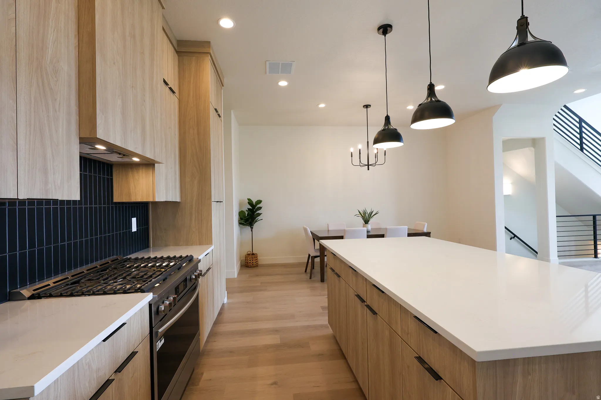 Kitchen featuring wood-finish cabinetry, a large center island with a light-toned countertop, a gas range with a tile backsplash, and recessed lighting