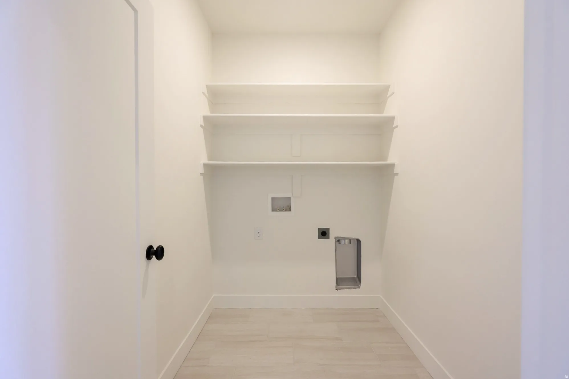 Utility closet featuring built-in shelving, light-toned tile flooring, and utility hookups
