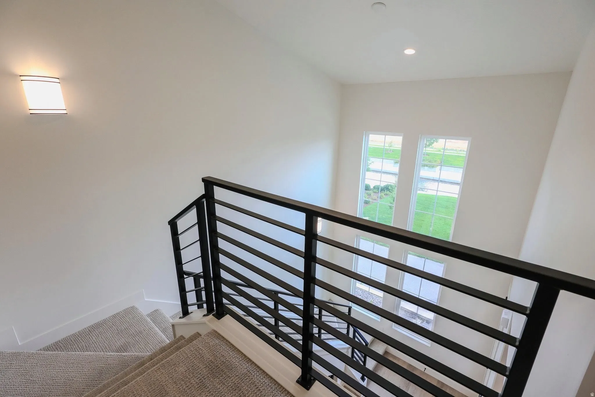 Staircase featuring horizontal bar railing, carpeted treads, and overhead lighting
