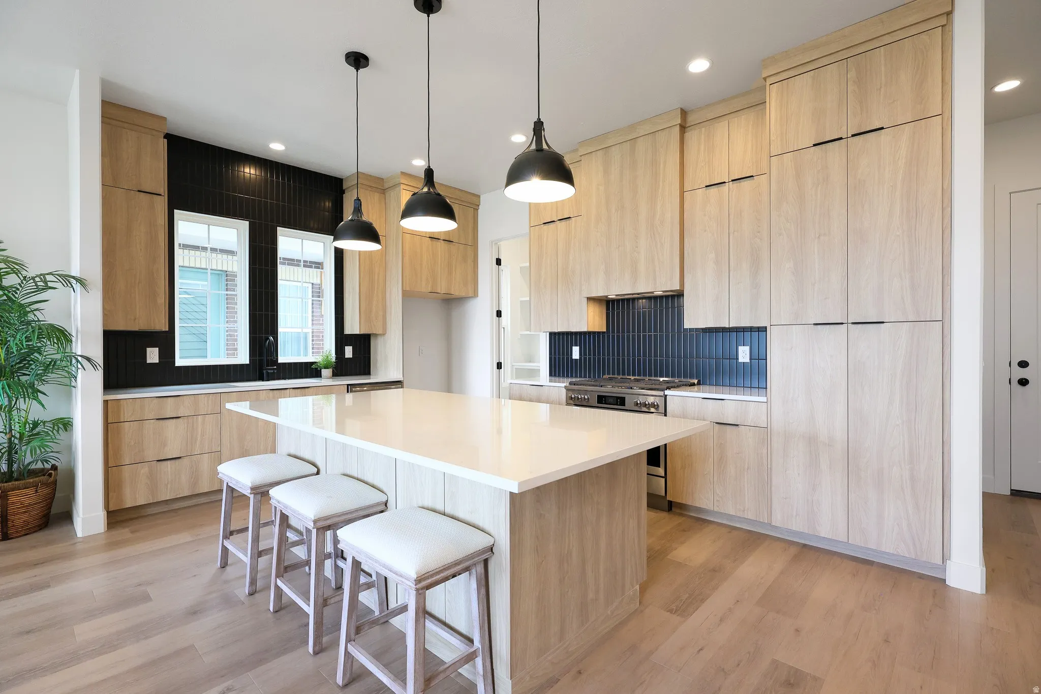 Gourmet kitchen with light wood-finish cabinetry, a large central island, black tile backsplash, and stainless steel appliances