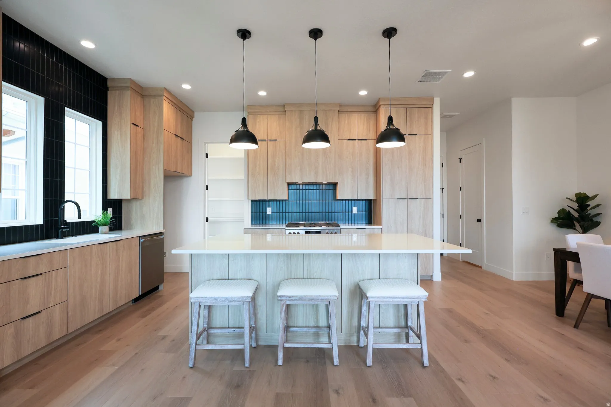 Modern kitchen featuring light wood-finish cabinetry, a large kitchen island with counter seating, stainless steel appliances, and a tiled backsplash