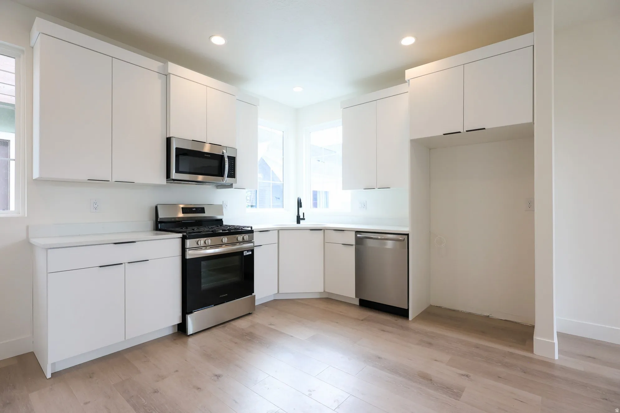 ADU-Modern kitchen featuring white cabinetry, light-toned wood-finish flooring, stainless steel appliances, and recessed lighting