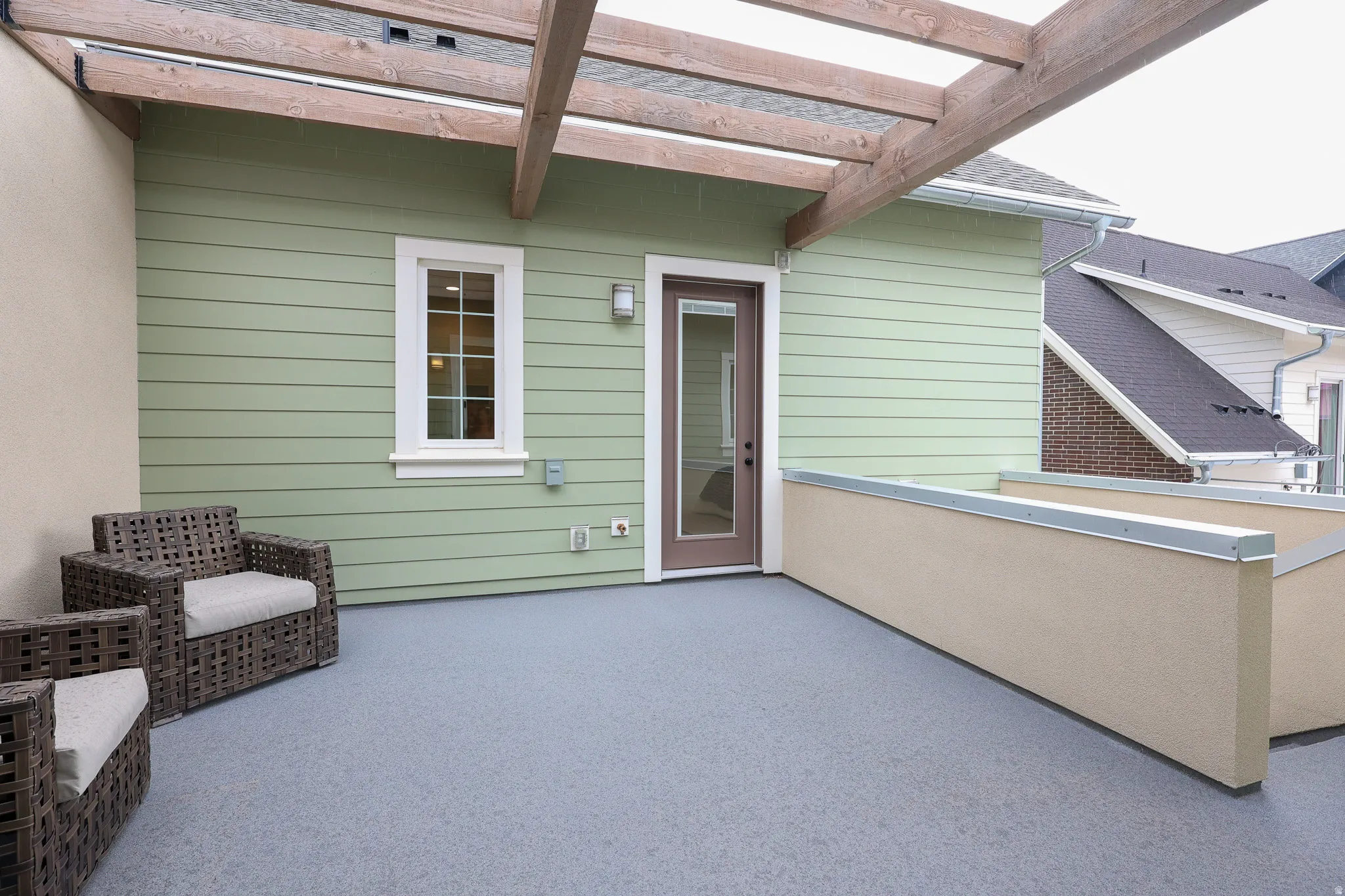 Outdoor terrace featuring a pergola, light green siding, and a neutral-toned privacy wall