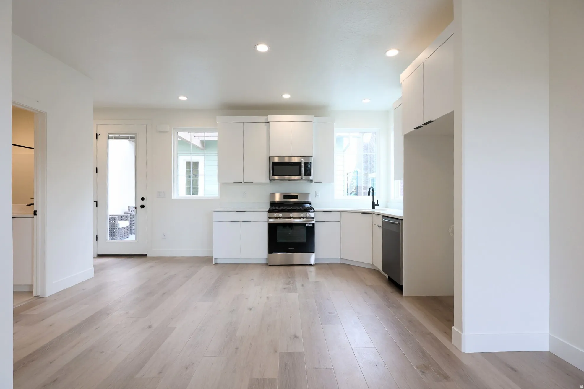 ADU-Kitchen with integrated stainless steel appliances, white cabinetry, recessed lighting, and wood-finish flooring