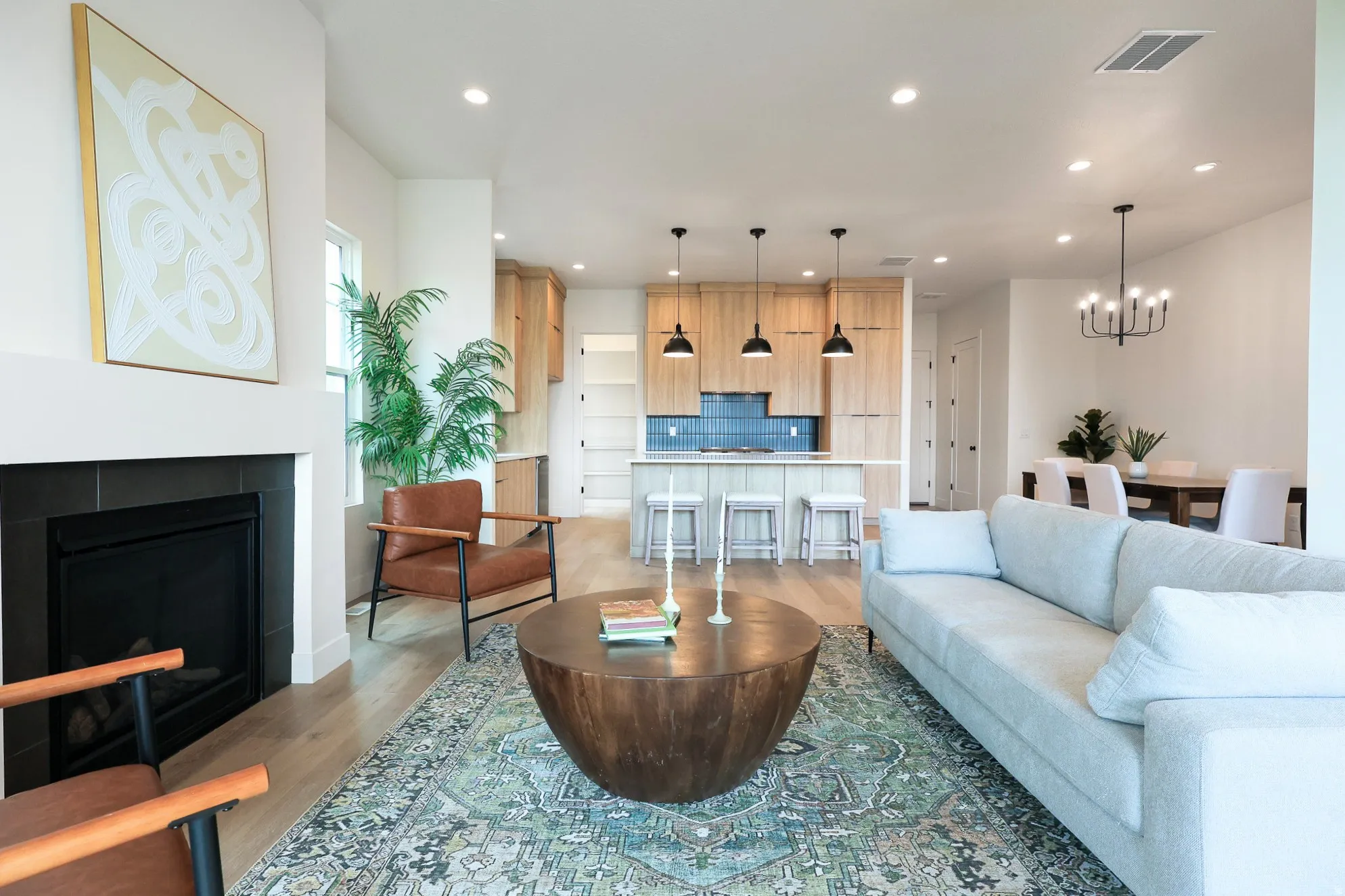 Open-concept living space featuring wood-finish flooring, a tiled fireplace, recessed lighting, and a kitchen island with pendant lighting