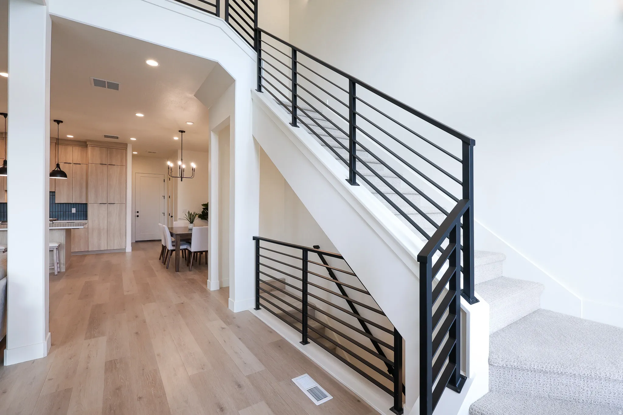 Two-story staircase with contemporary black metal railings, light wood-finish flooring, recessed lighting, and a modern chandelier